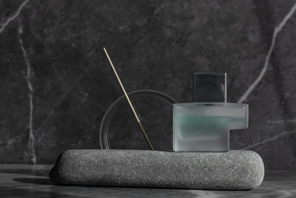 Elegant still life: perfume bottle, marble, incense, and geometric shapes in grayscale.